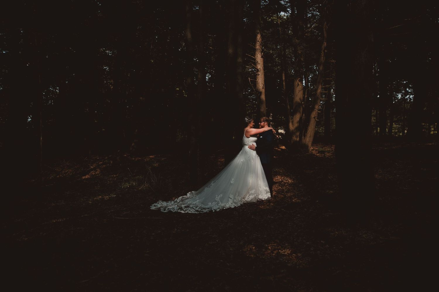 A couple in wedding attire photographed in a dark, atmospheric forest setting. wedding