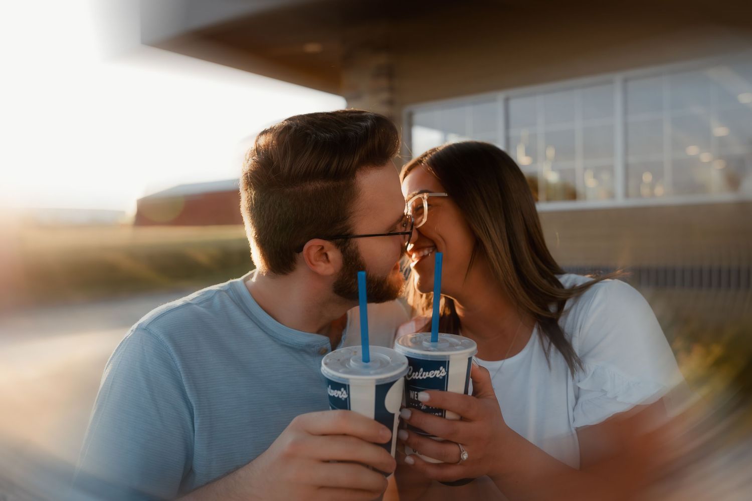 Happy couple sharing milkshakes and kissing at Culvers restaurant during sunset.