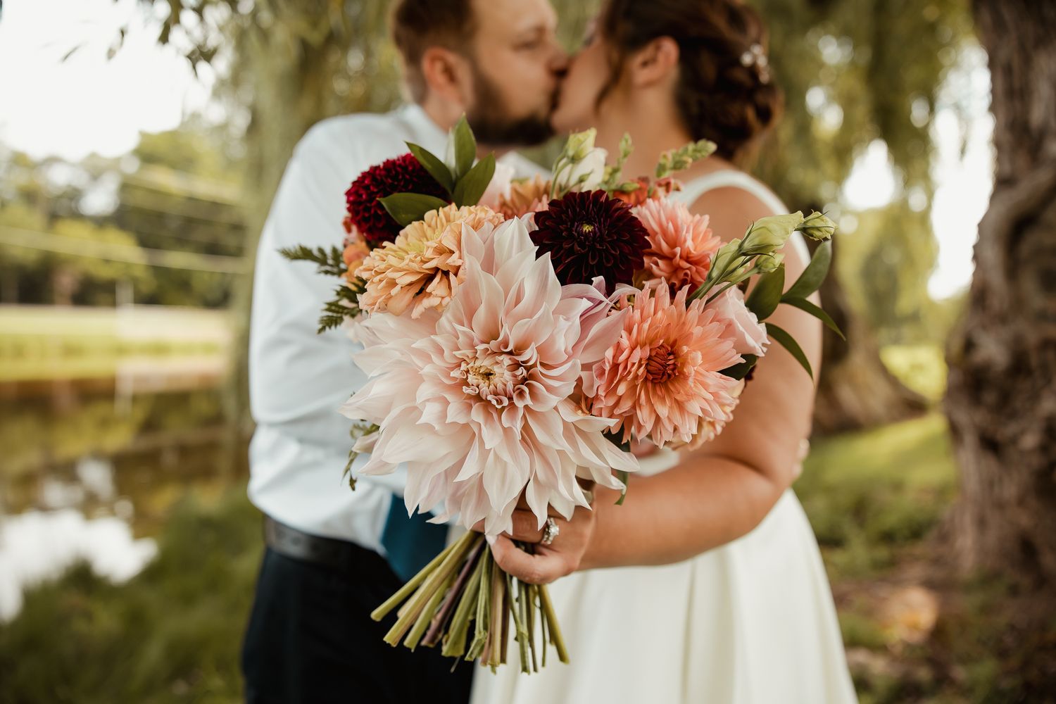 A romantic outdoor wedding celebration with soft pink and burgundy floral bouquets against a natural garden backdrop.
