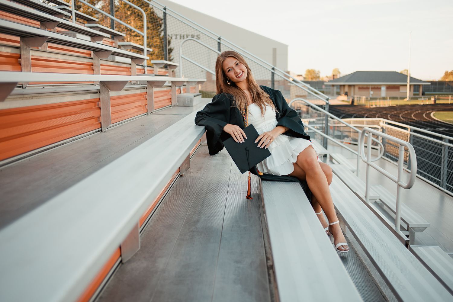 Young stylish woman in black outfit posing confidently on modern architectural railings at sunset.