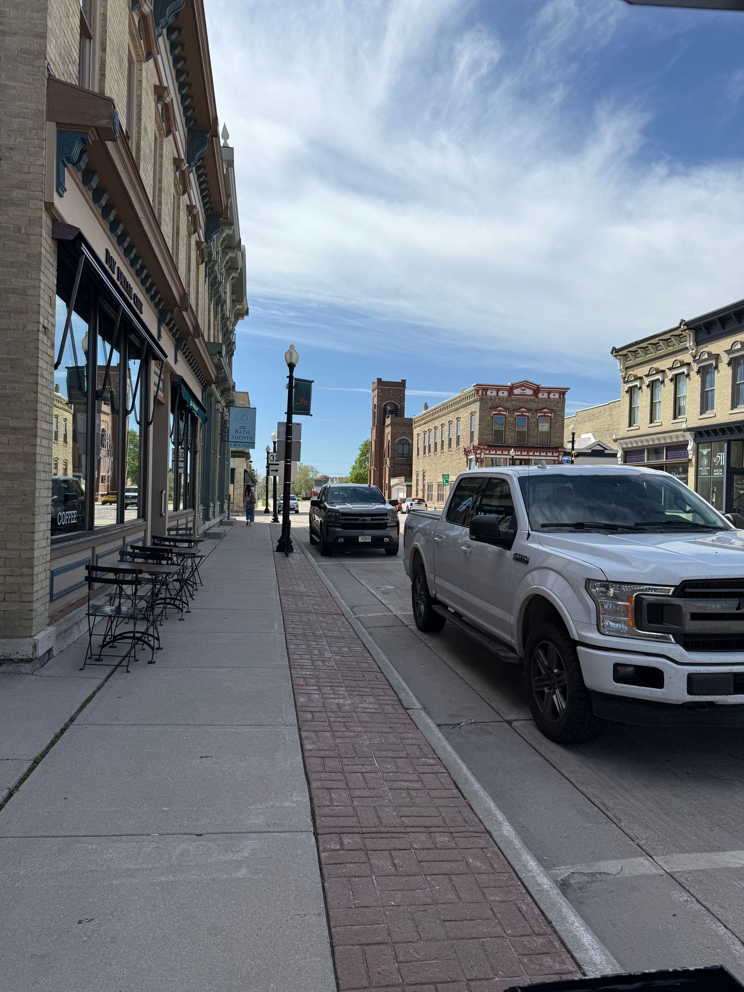 A small town main street lined with historic brick buildings, parked trucks, and metal street lamps on a sunny day.