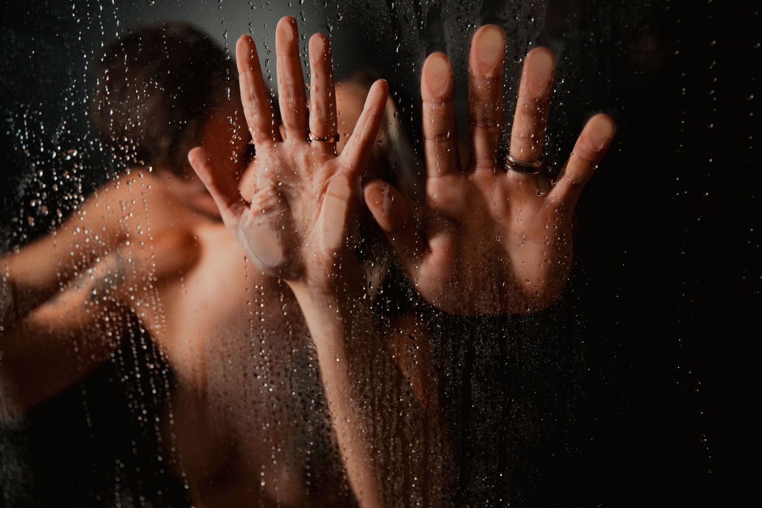 Dark moody shadows of hands pressed against frosted glass casting dramatic silhouettes in black and white.