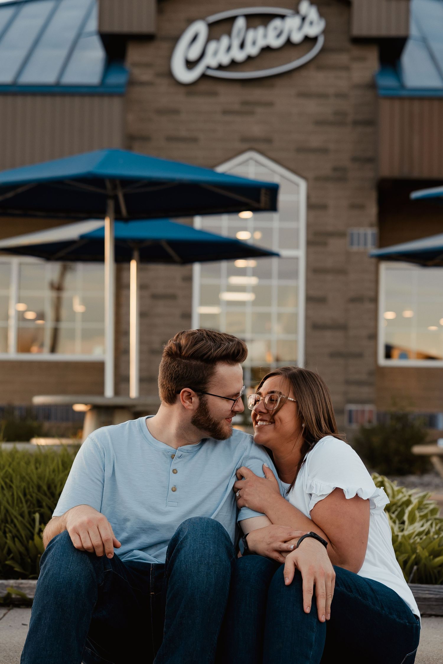 A loving couple sitting close together outside a Culvers restaurant at dusk.