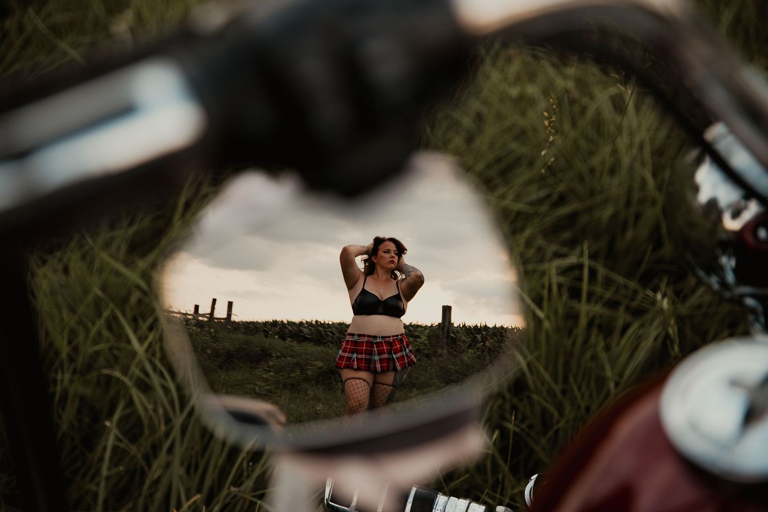 Creative reflection in motorcycle mirror shows photographer taking picture in grassy field at sunset.