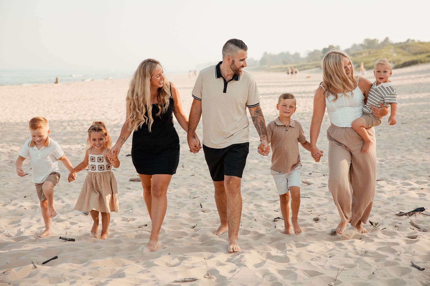 Family of seven walking on sandy beach at sunset, parents holding hands with children in casual summer outfits.