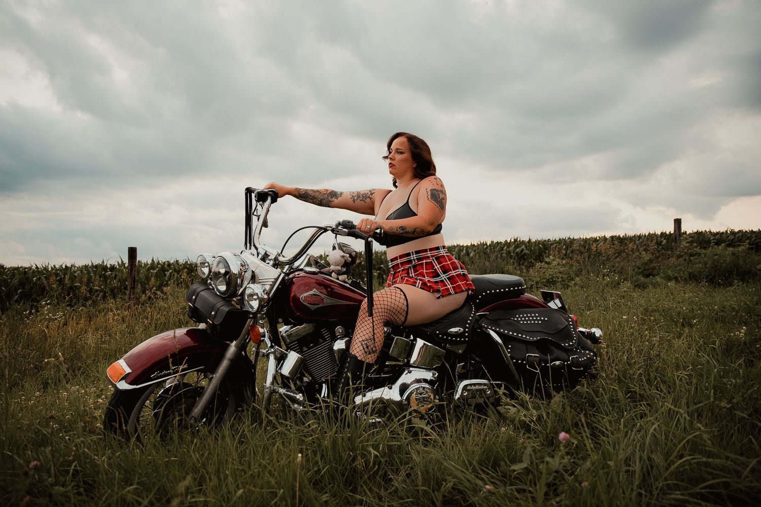 A vintage motorcycle sits parked in a grassy meadow under dramatic cloudy skies during a summer photoshoot.