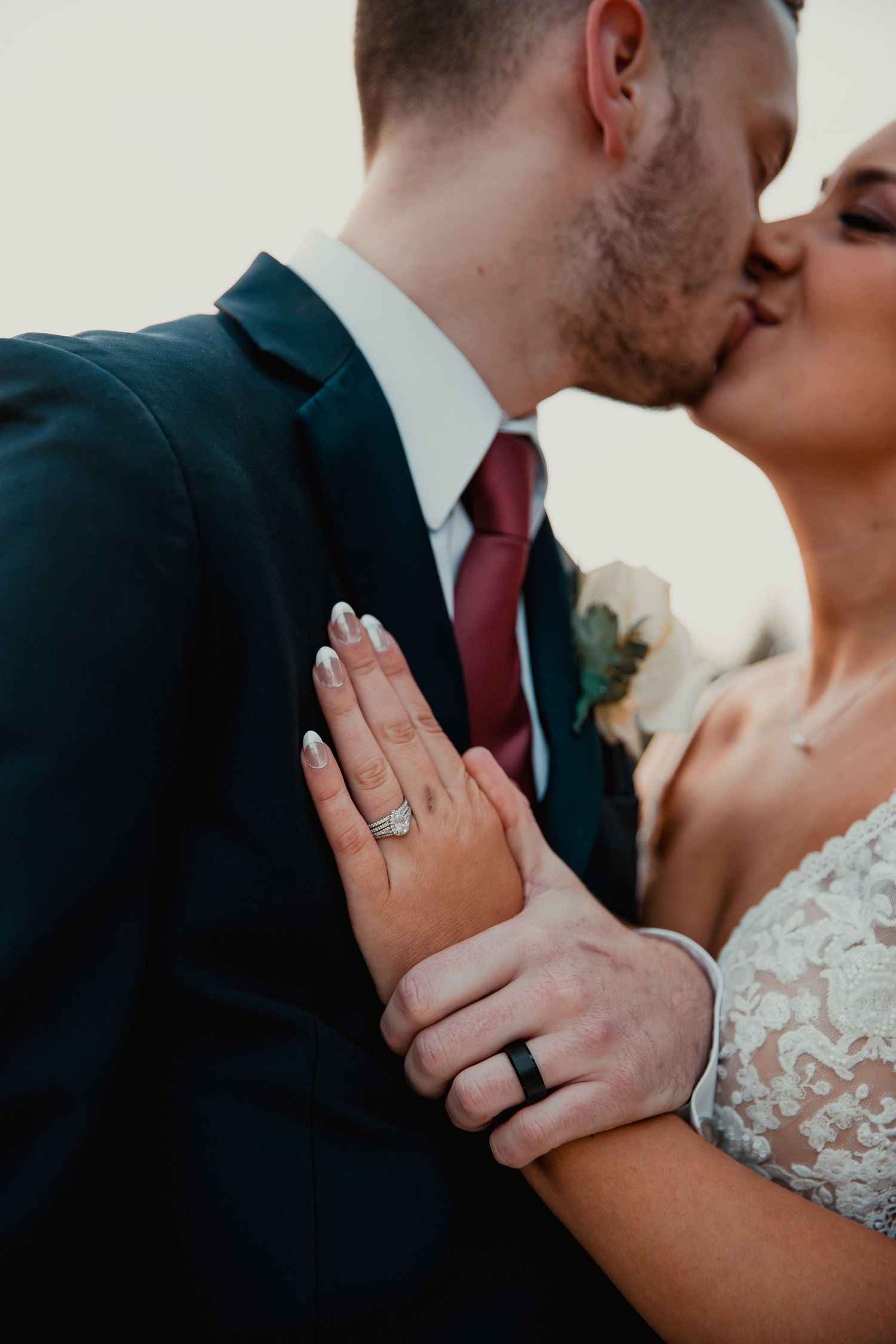 Close-up of wedding rings and hands with lace dress and navy suit details. wedding