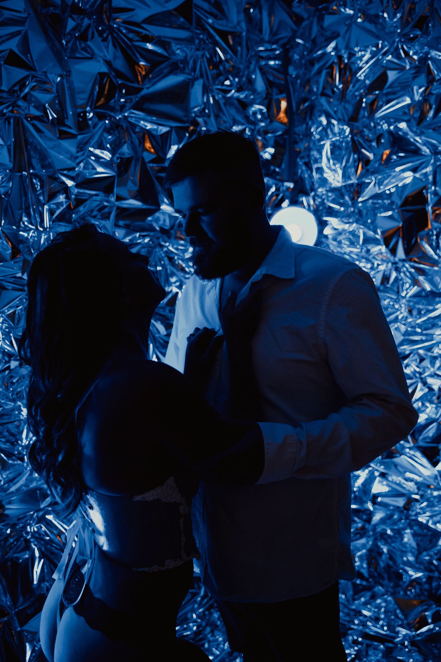 Silhouettes of figures against a backdrop of shimmering blue metallic textures and reflective surfaces.