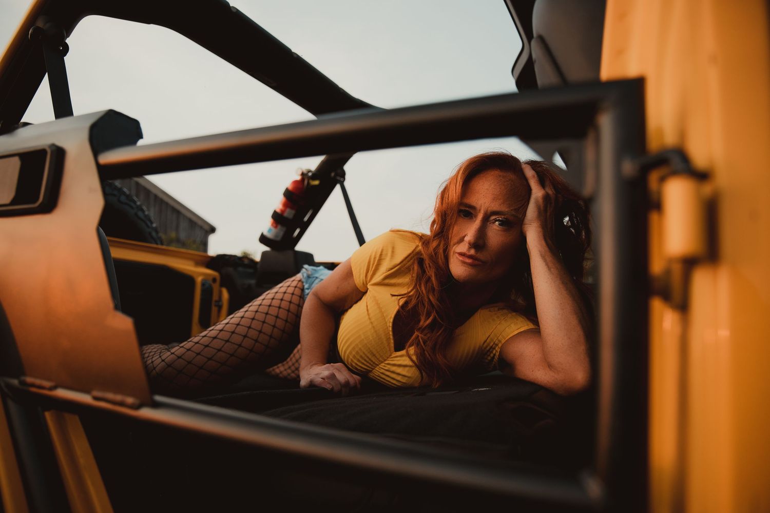 Candid photo through car window showing someone in a yellow top reclining on brown leather seats at sunset.