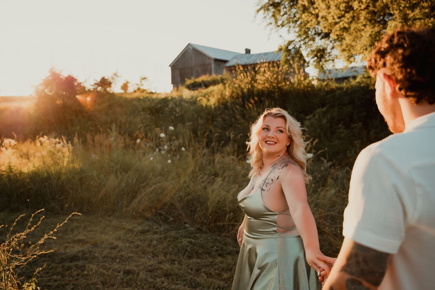 Dancing together in sunlit meadow with rustic farmhouse in background. couples engagement