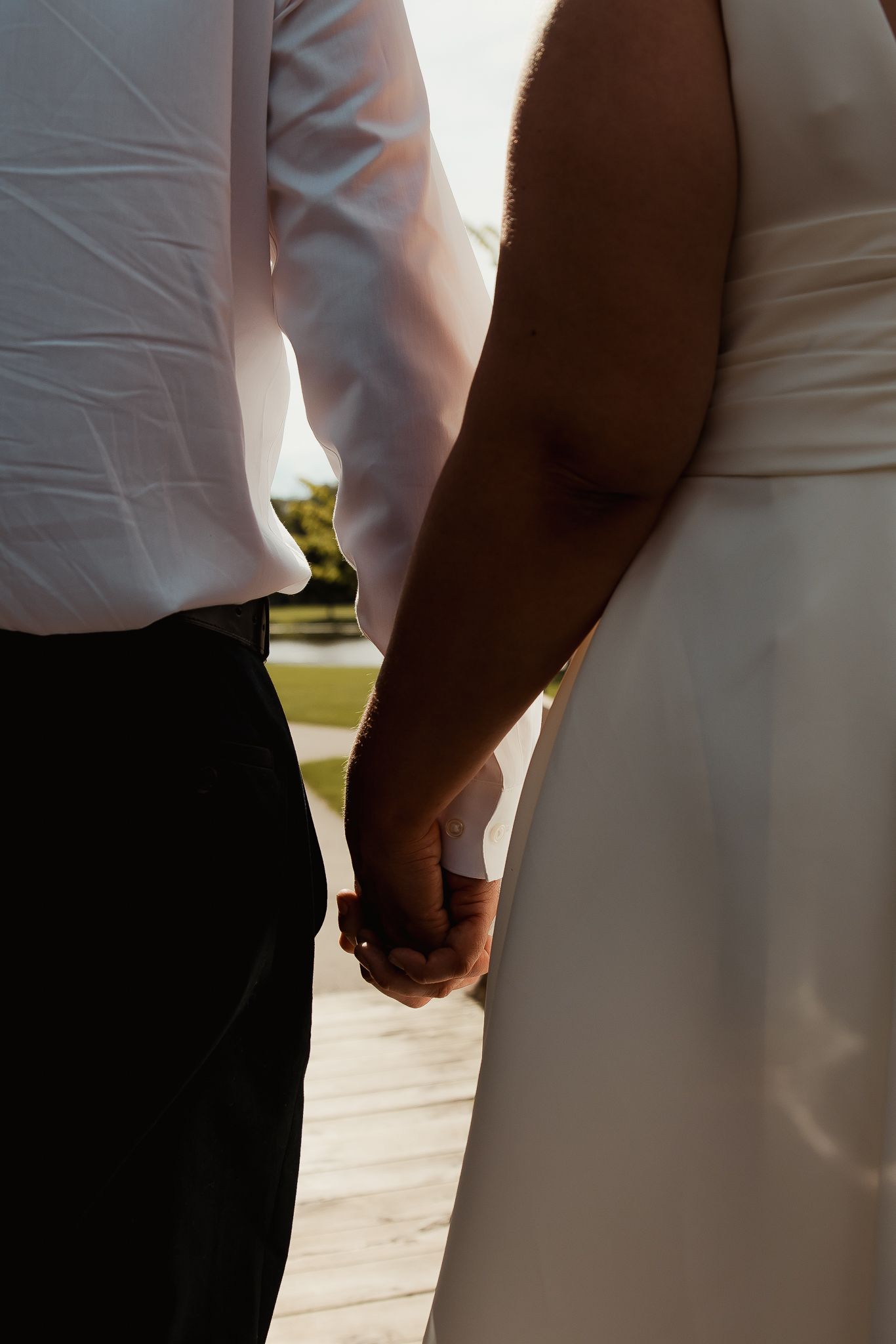 Close-up of an interracial couple holding hands, with one person in a white dress and another in black pants.