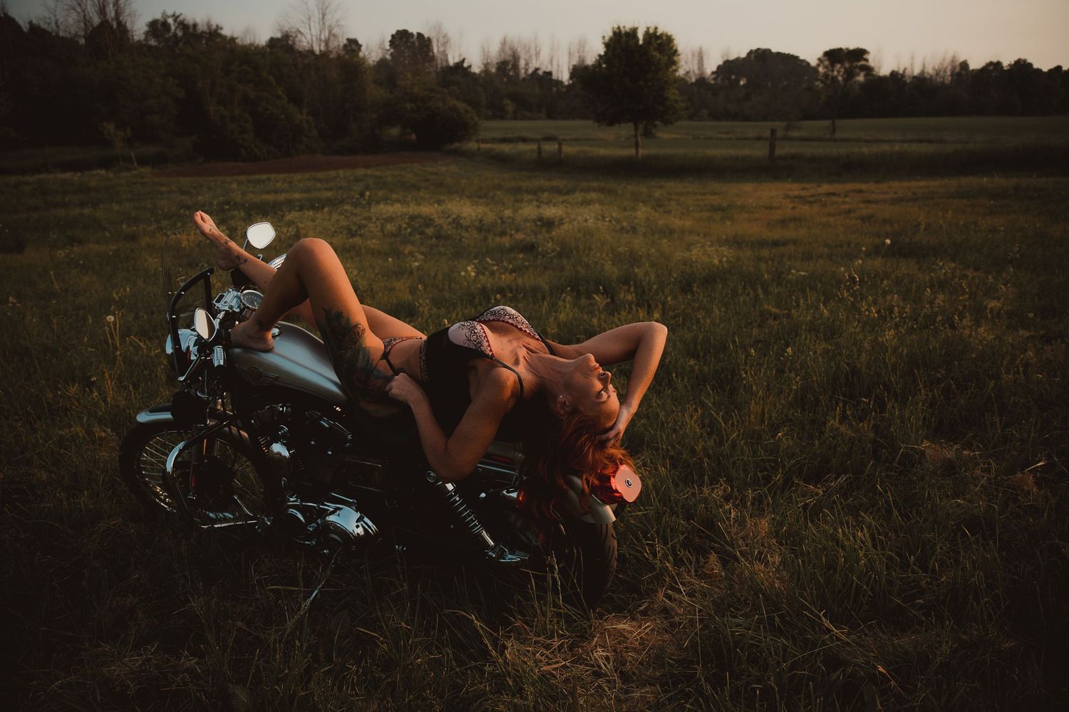 Someone relaxes on a motorcycle in a serene meadow at sunset.