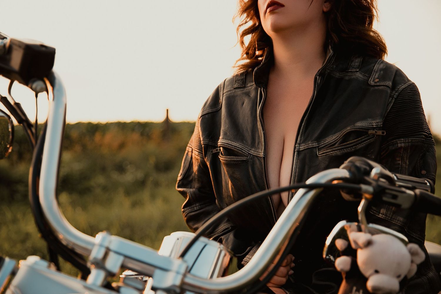 Close-up view of chrome motorcycle handlebars with leather jacket in golden sunset light.