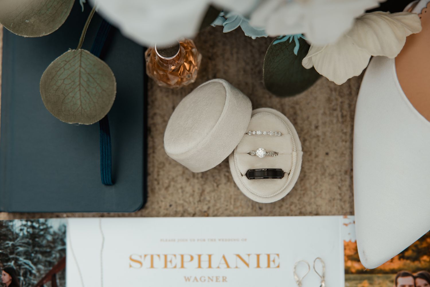 Wedding details arranged on table including a white jewelry case and gold foil lettering invitation.