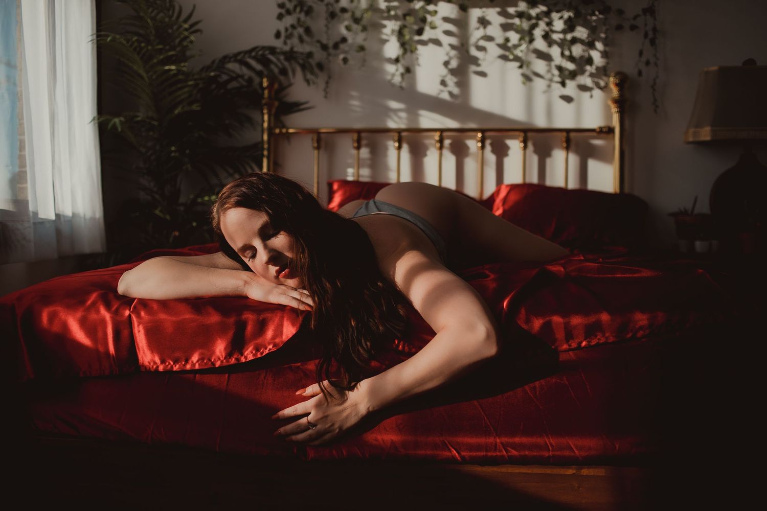A series of dark and moody boudoir photos with red lighting and dramatic shadows on a bed.