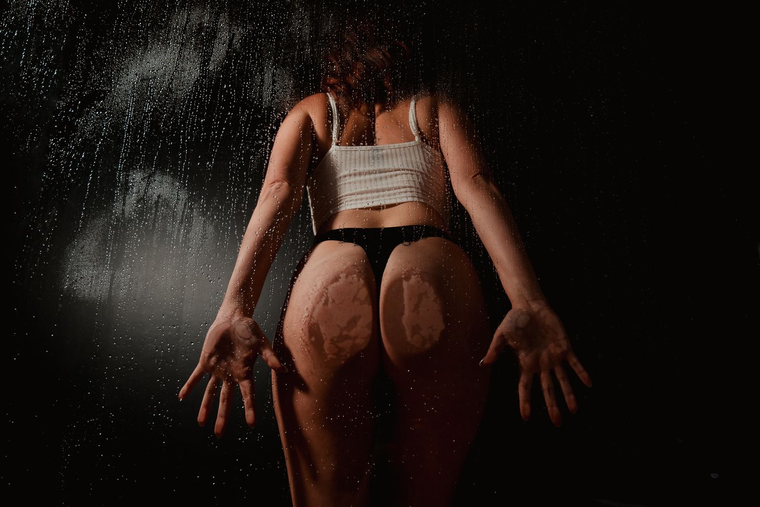 Dramatic artistic photo of a person in athletic wear against dark background with moody lighting and rain effects.