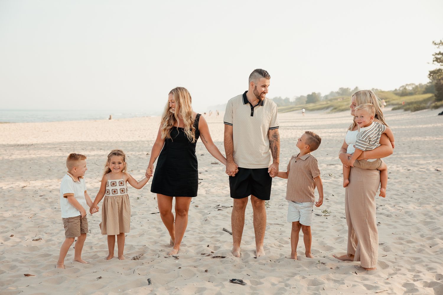 Family of six holding hands and walking on a sandy beach on a sunny day.