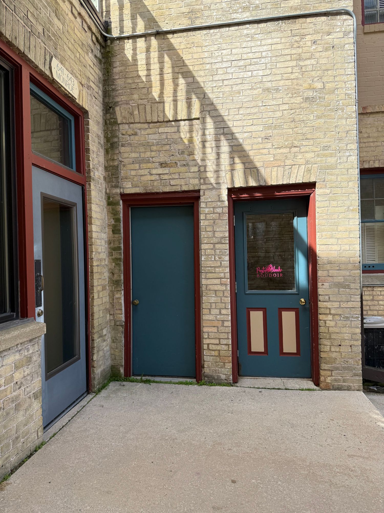 Two dark blue doors with red trim frame set against a light brick wall with diagonal shadows cast across the surface.