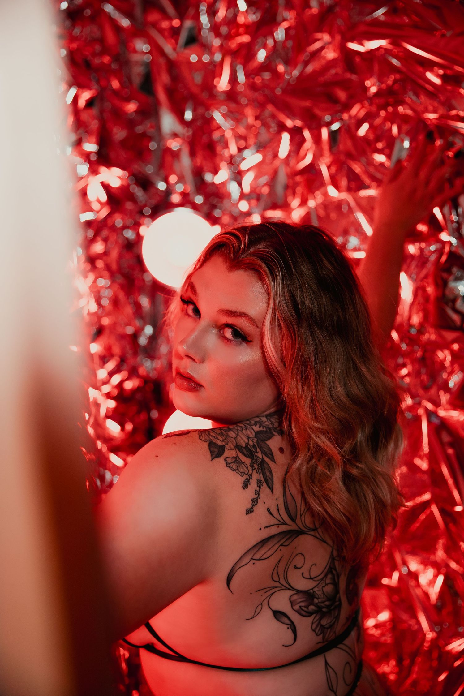 Artistic portrait against vibrant red metallic backdrop with dramatic lighting and neck tattoo detail.