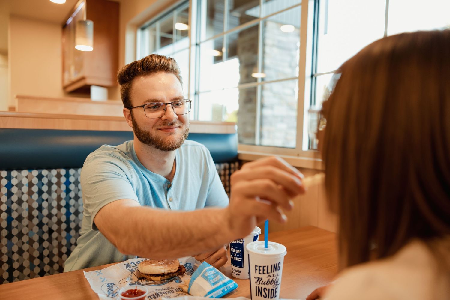 Man smiling at woman while sharing a meal at Culver's restaurant booth with burgers and drinks.