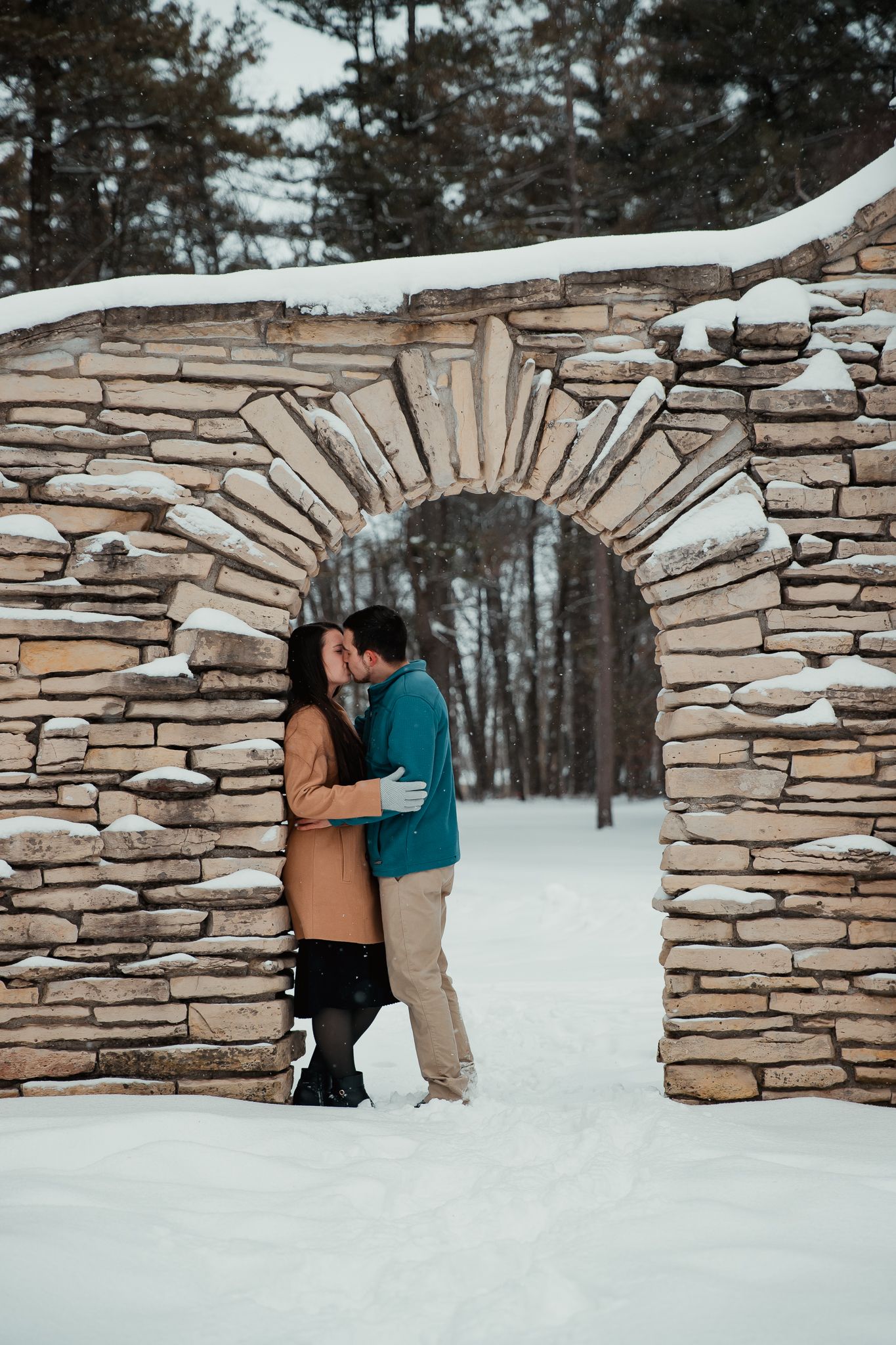 A romantic moment under a stone archway in a snowy winter setting. couples engagement