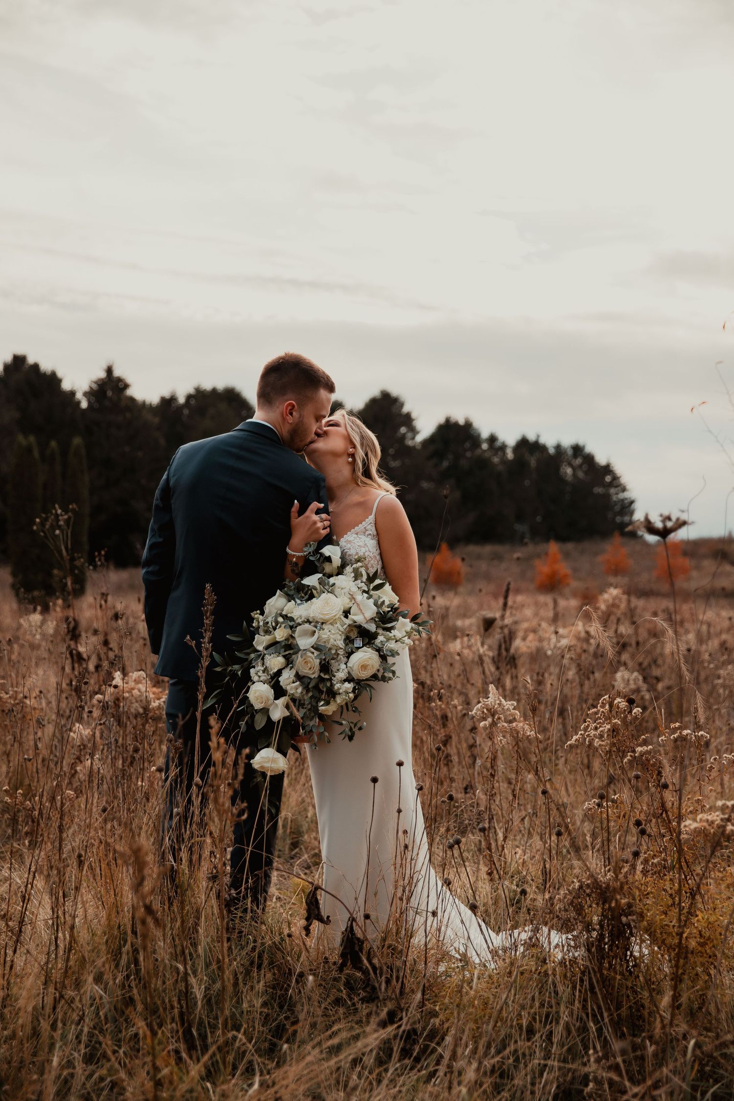 Intimate wedding portrait in rustic field with white floral bouquet at sunset. wedding