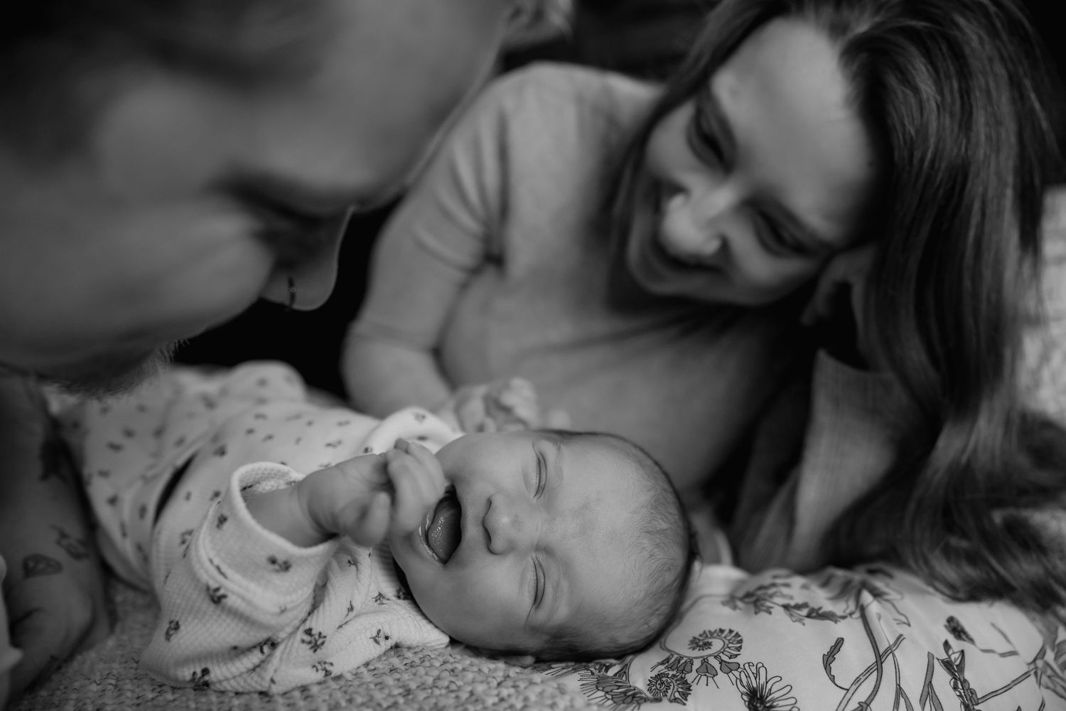 Black and white photo of a sleeping baby swaddled in floral blanket laying on bed.