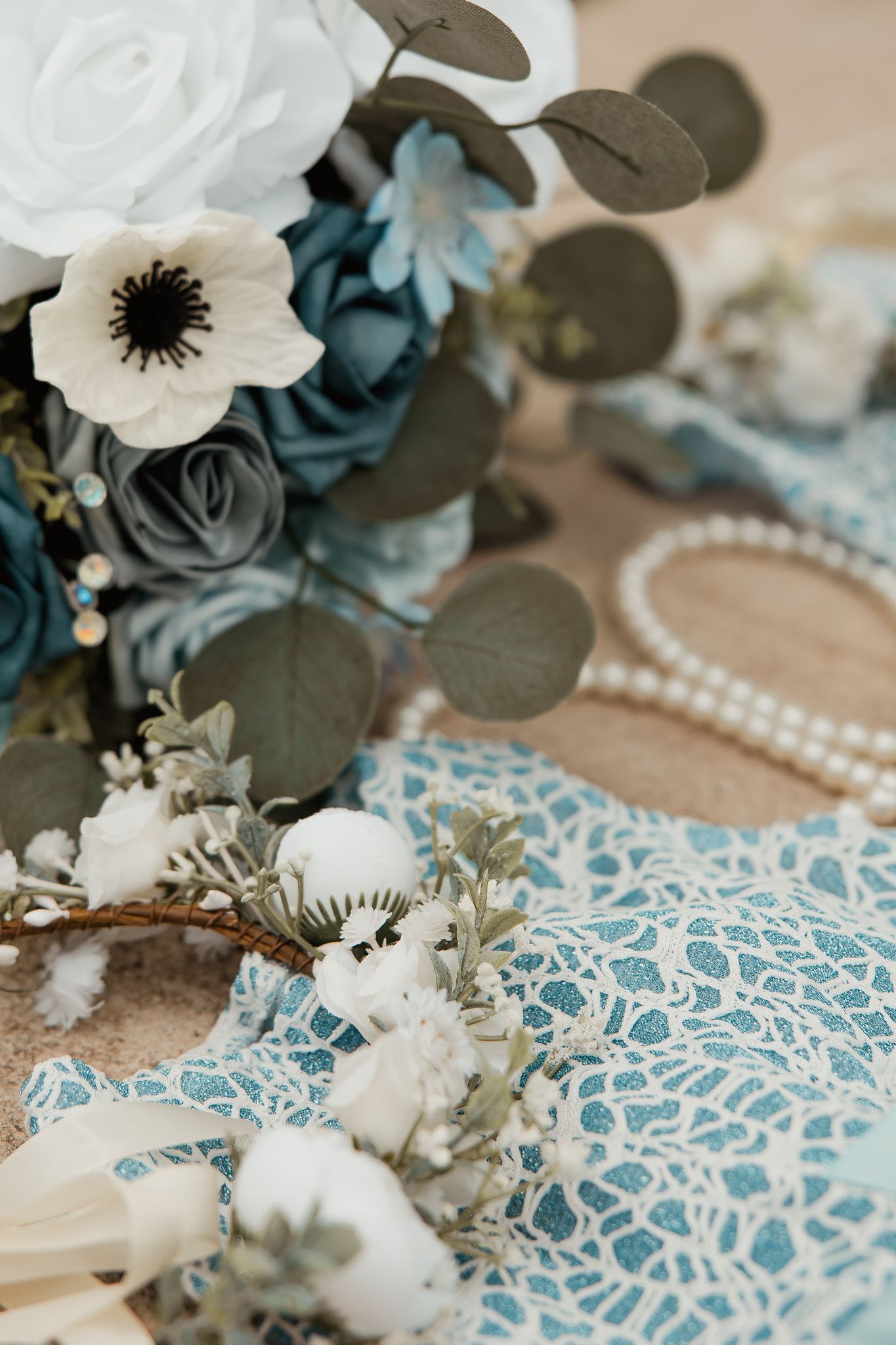 An elegant floral arrangement with white anemones and dusty blue roses alongside delicate lace and pearl details.