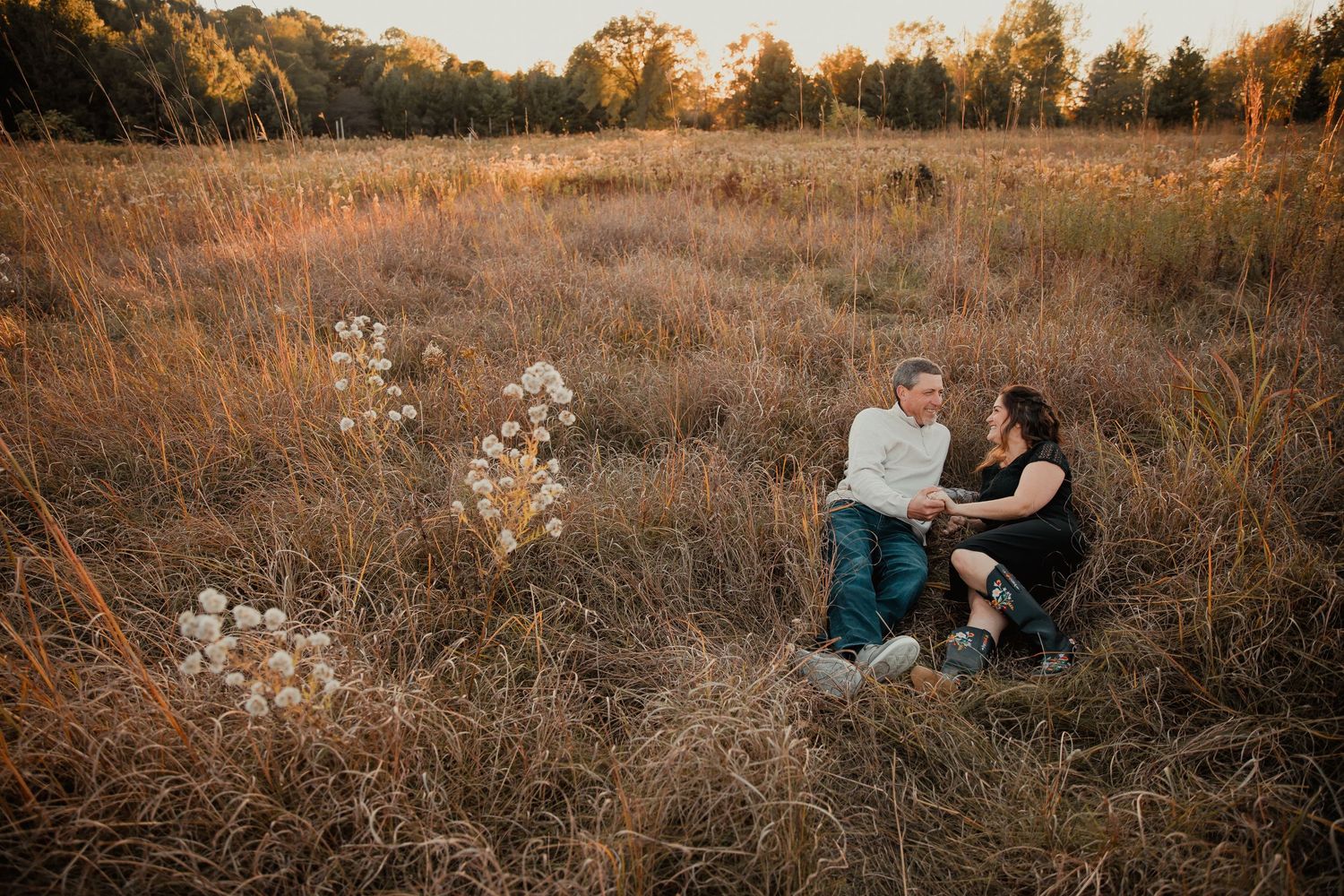 A couple sits together in a serene autumn field surrounded by golden grass at sunset. couples engagement