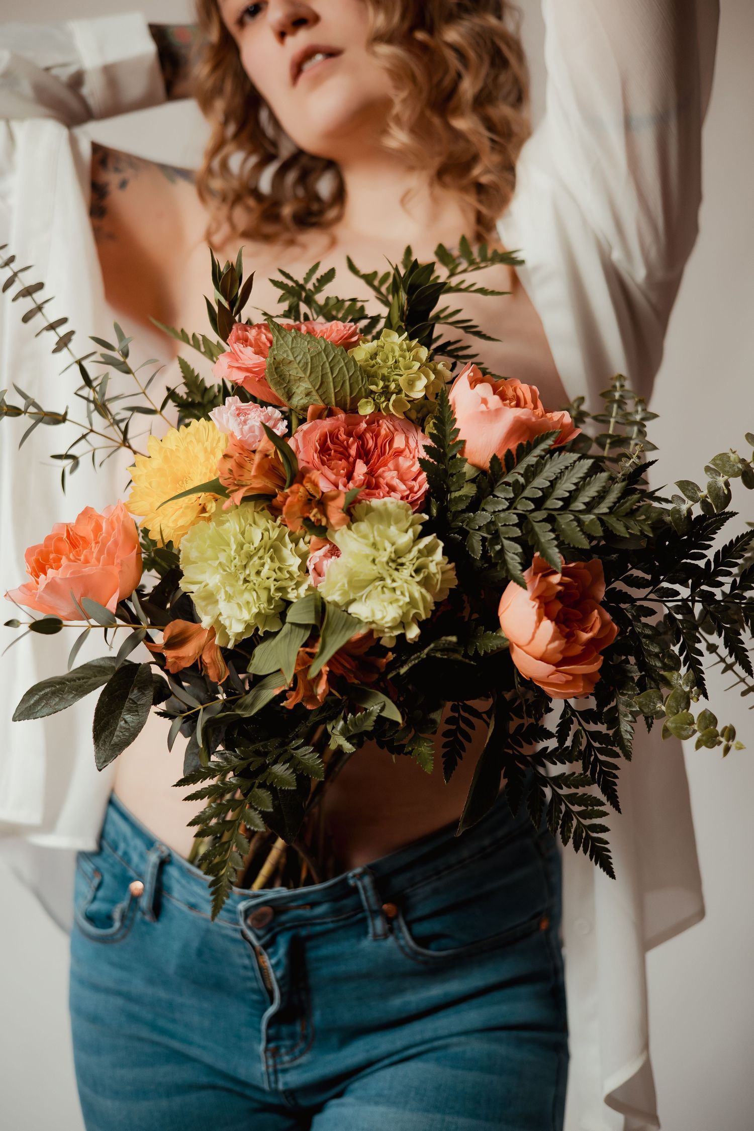 A person in blue jeans holds a beautiful bouquet of peach roses, green hydrangeas and ferns against a white background.