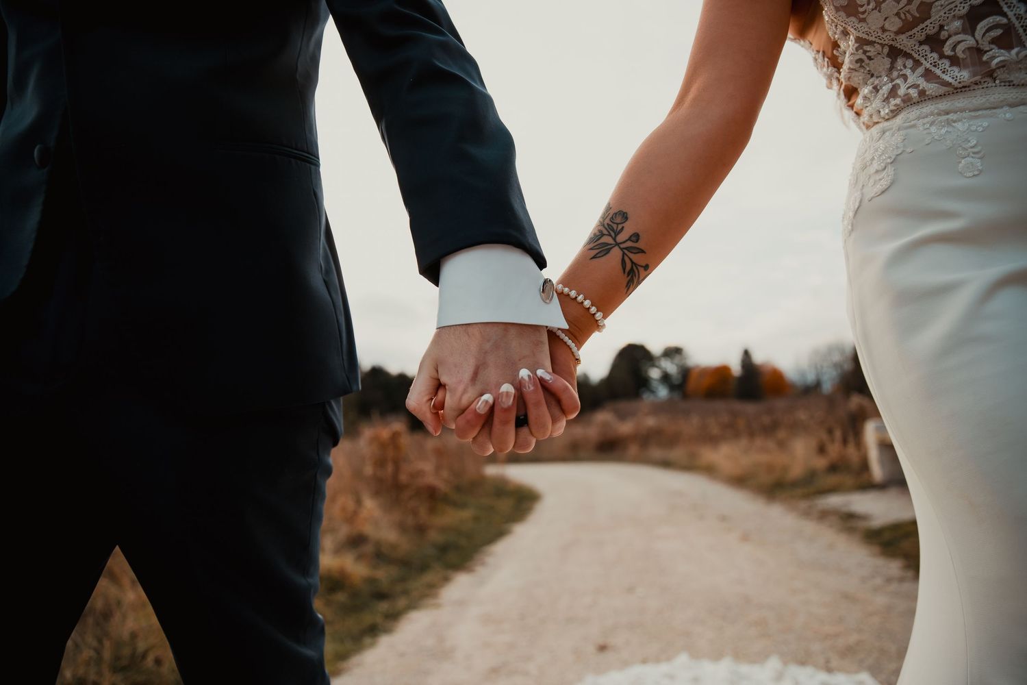 A couple holding hands while walking down a dirt path at sunset. wedding