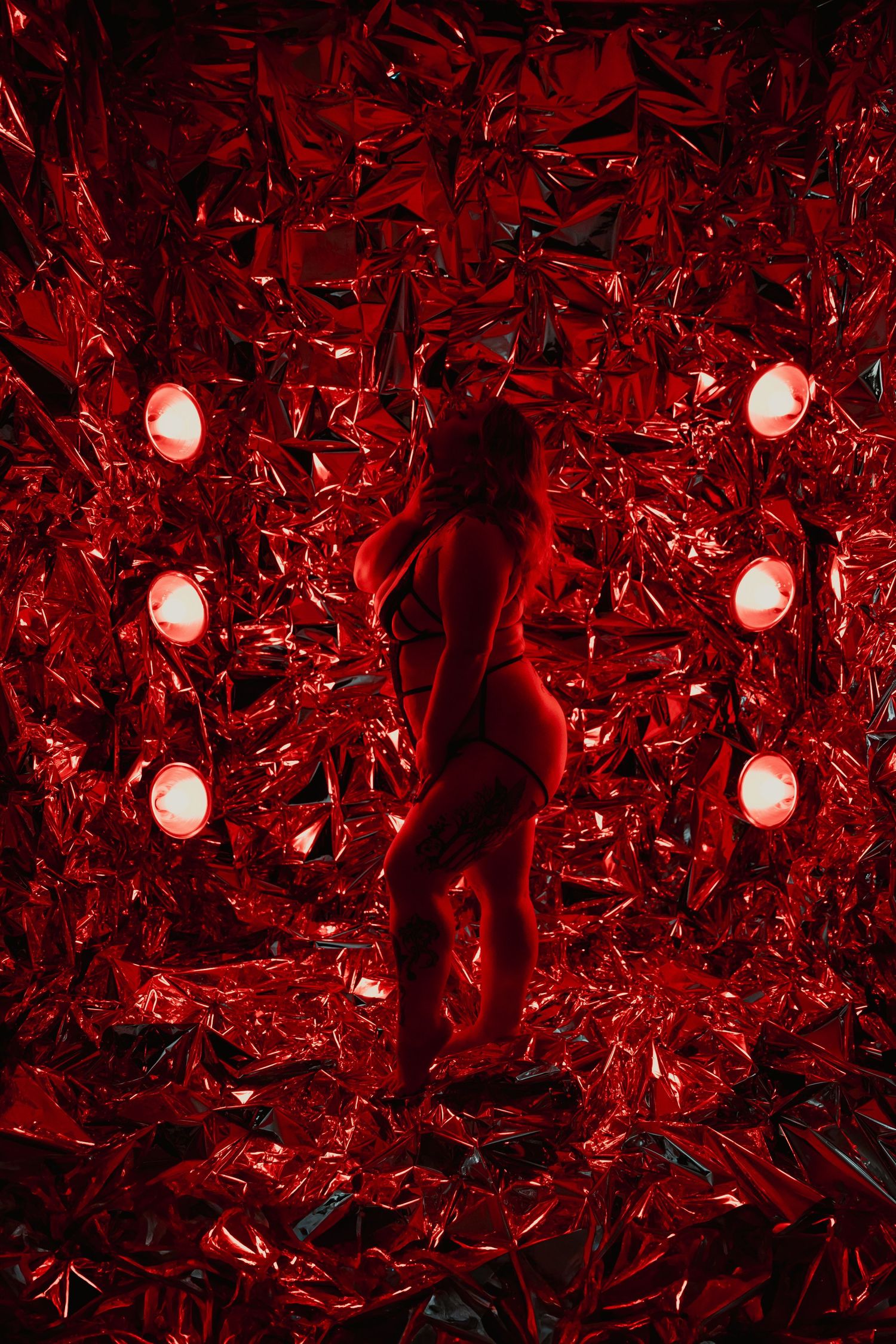 A silhouette stands amid shattered red glass and illuminated orbs creating a dramatic artistic installation.