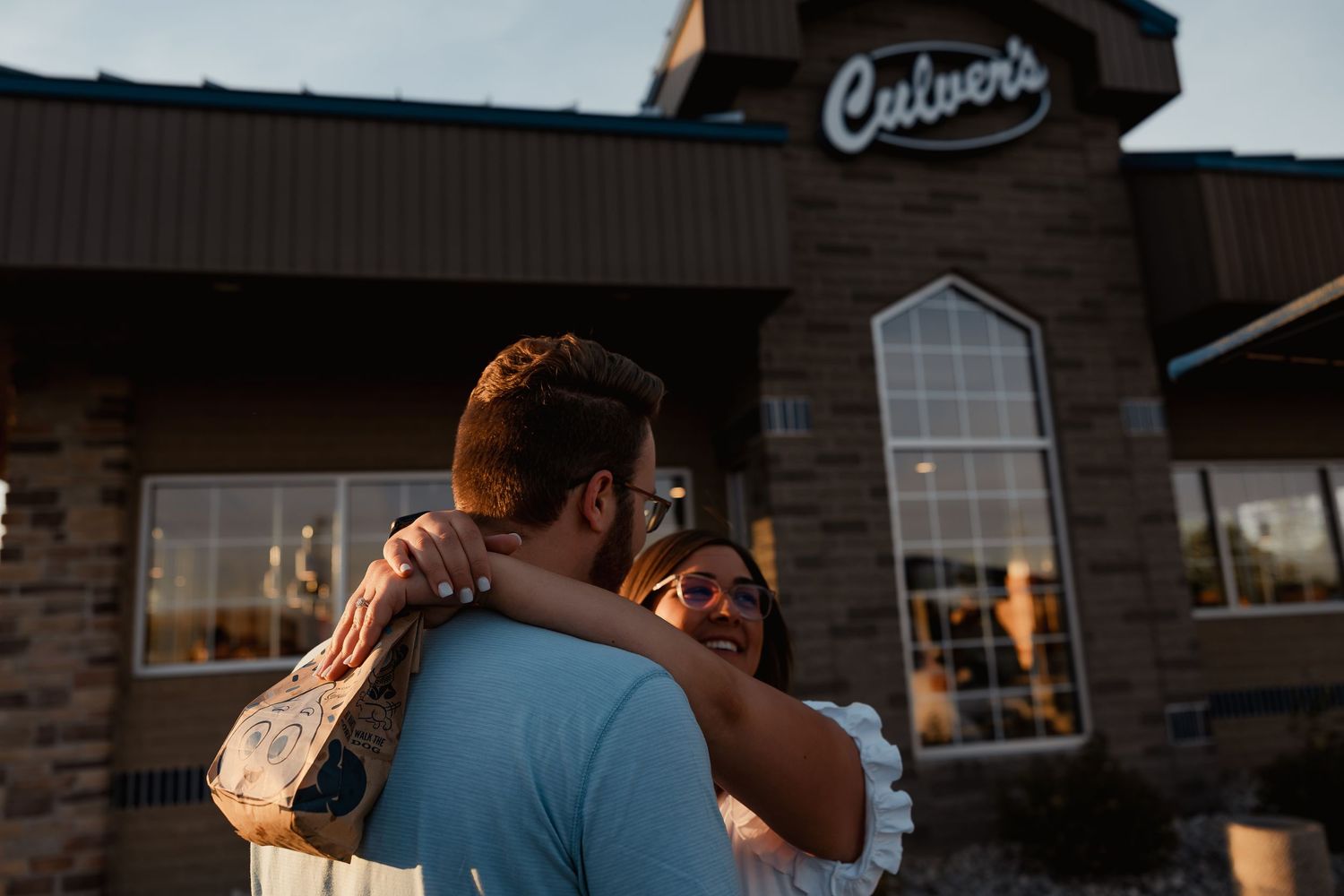 A happy couple embracing outside a Culvers restaurant at golden hour sunset.