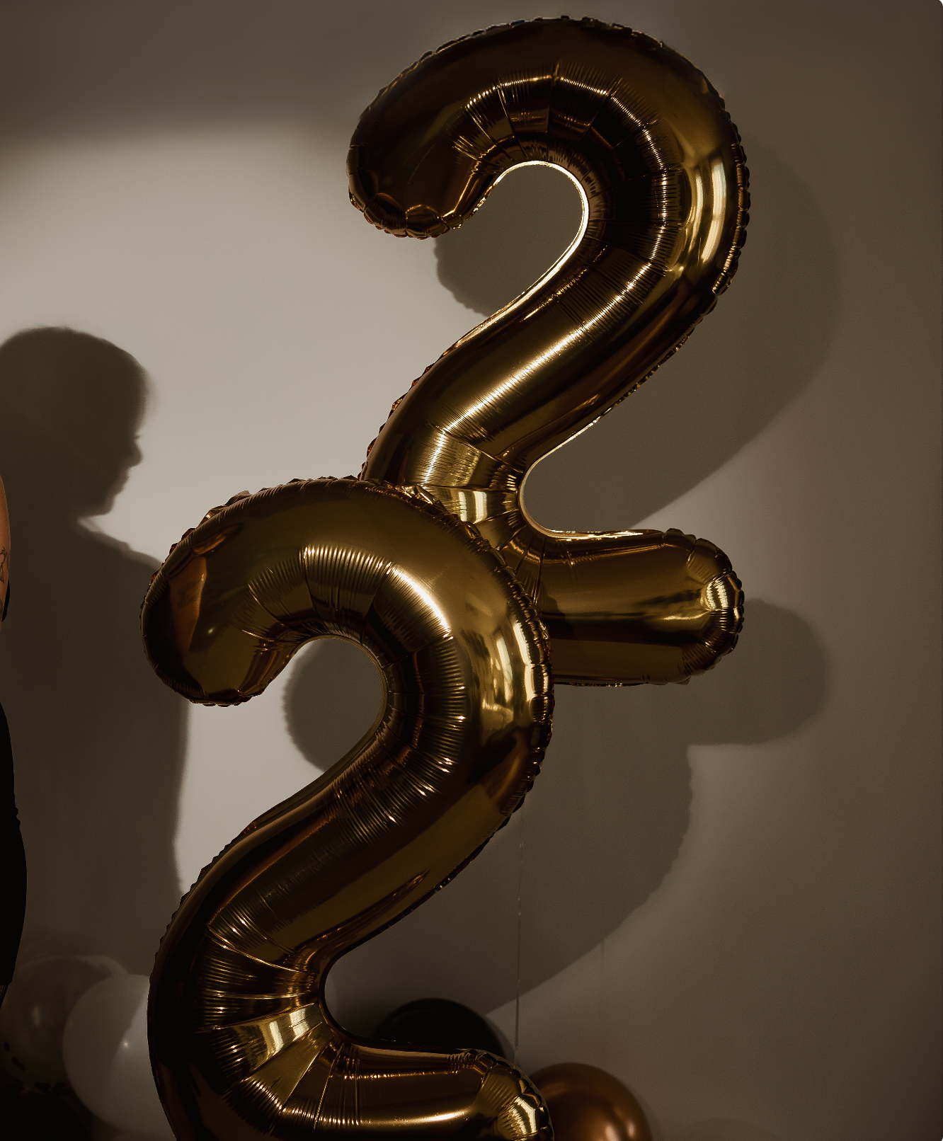 Gold metallic number 32 foil balloons against a white wall for a birthday celebration.