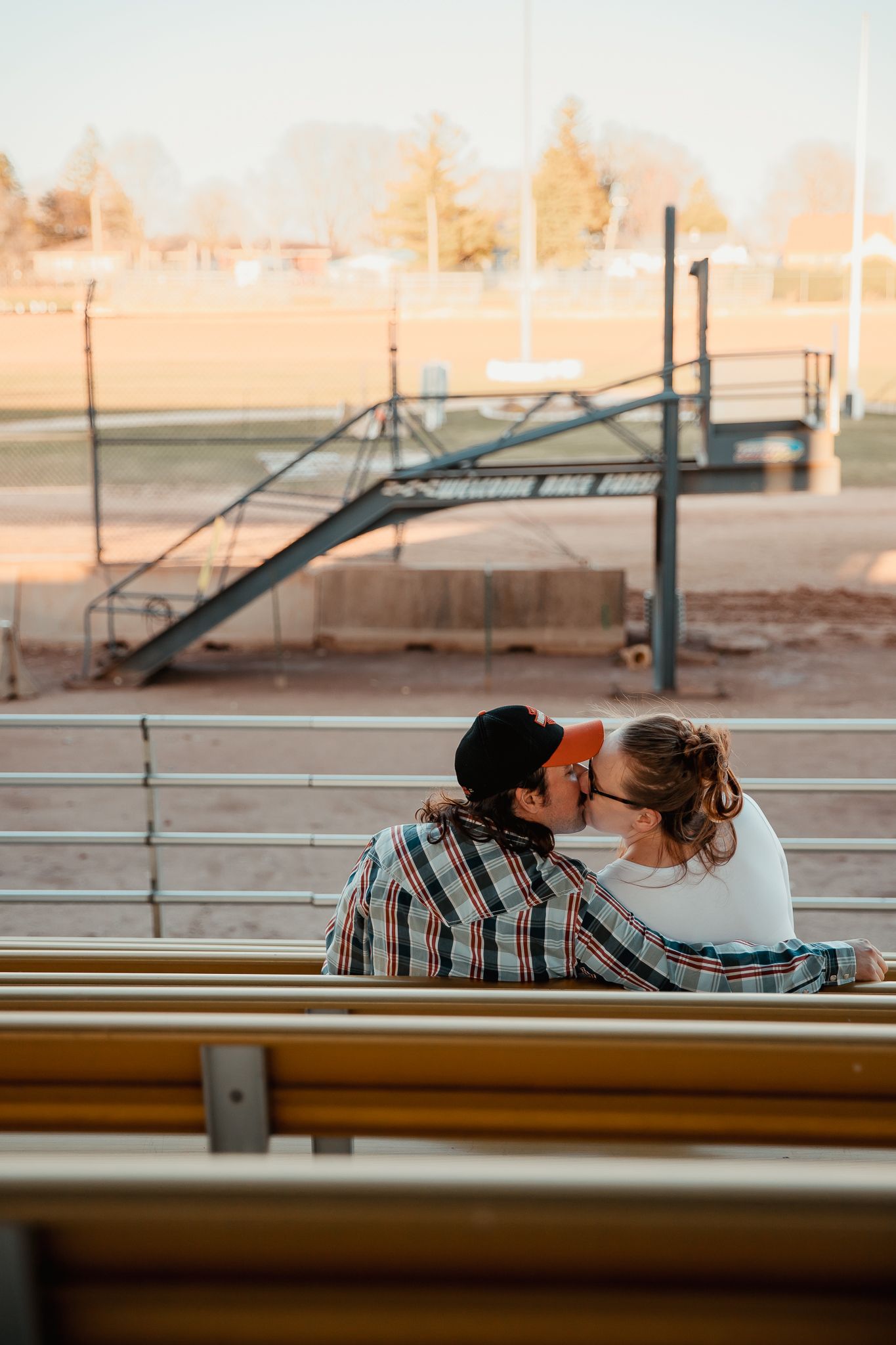 A couple shares a sunset kiss on bleacher seating at an outdoor venue. couples engagement maternity