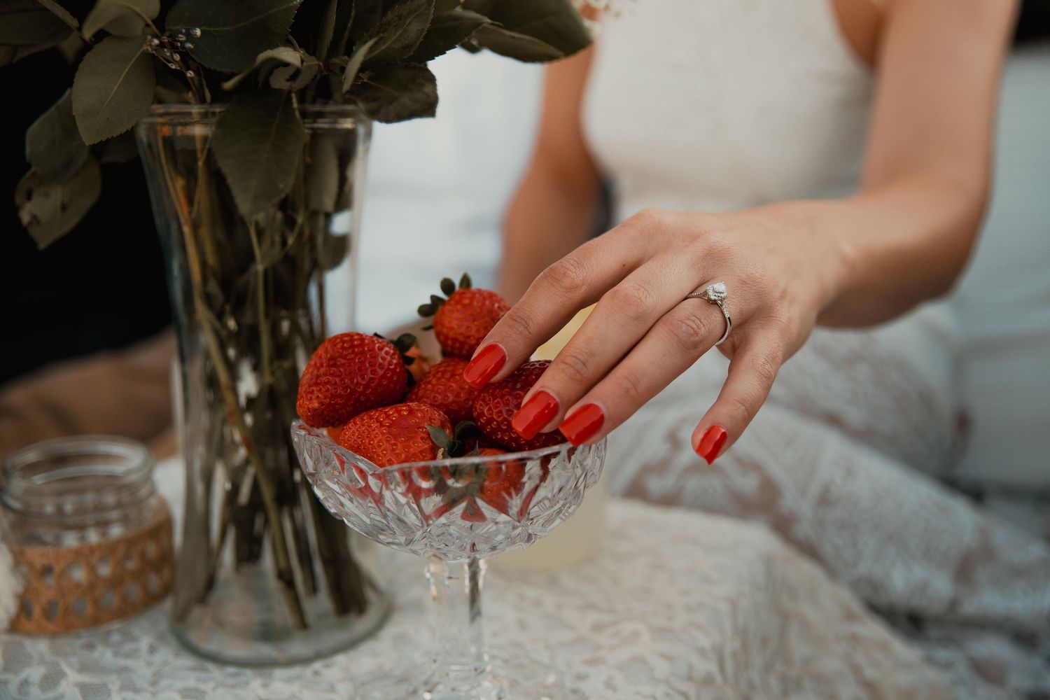 A delicate hand with red nails and engagement ring reaches for fresh strawberries in a crystal bowl. wedding engagement couple