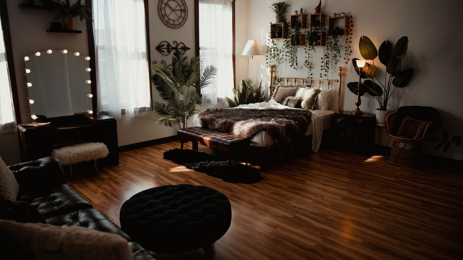 A cozy bedroom with warm lighting features wooden floors, plants, a vanity mirror, and modern bohemian decor.