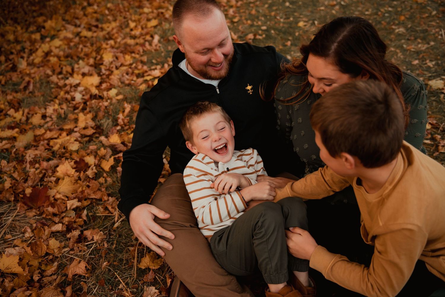 Family enjoying playful moments together outdoors during autumn with fallen leaves and warm earth tones.