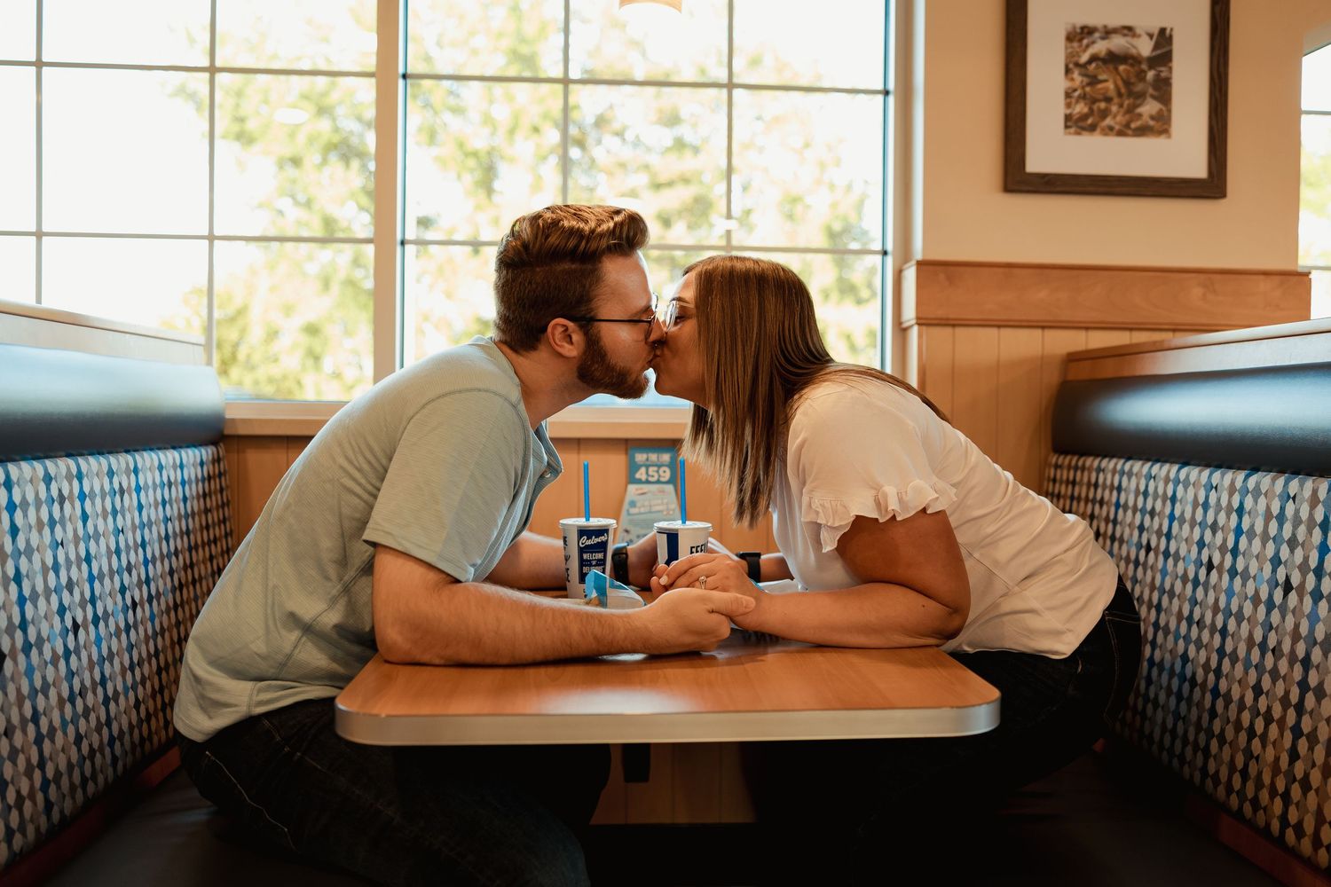 Couple sharing a romantic kiss at a diner booth by a sunny window.