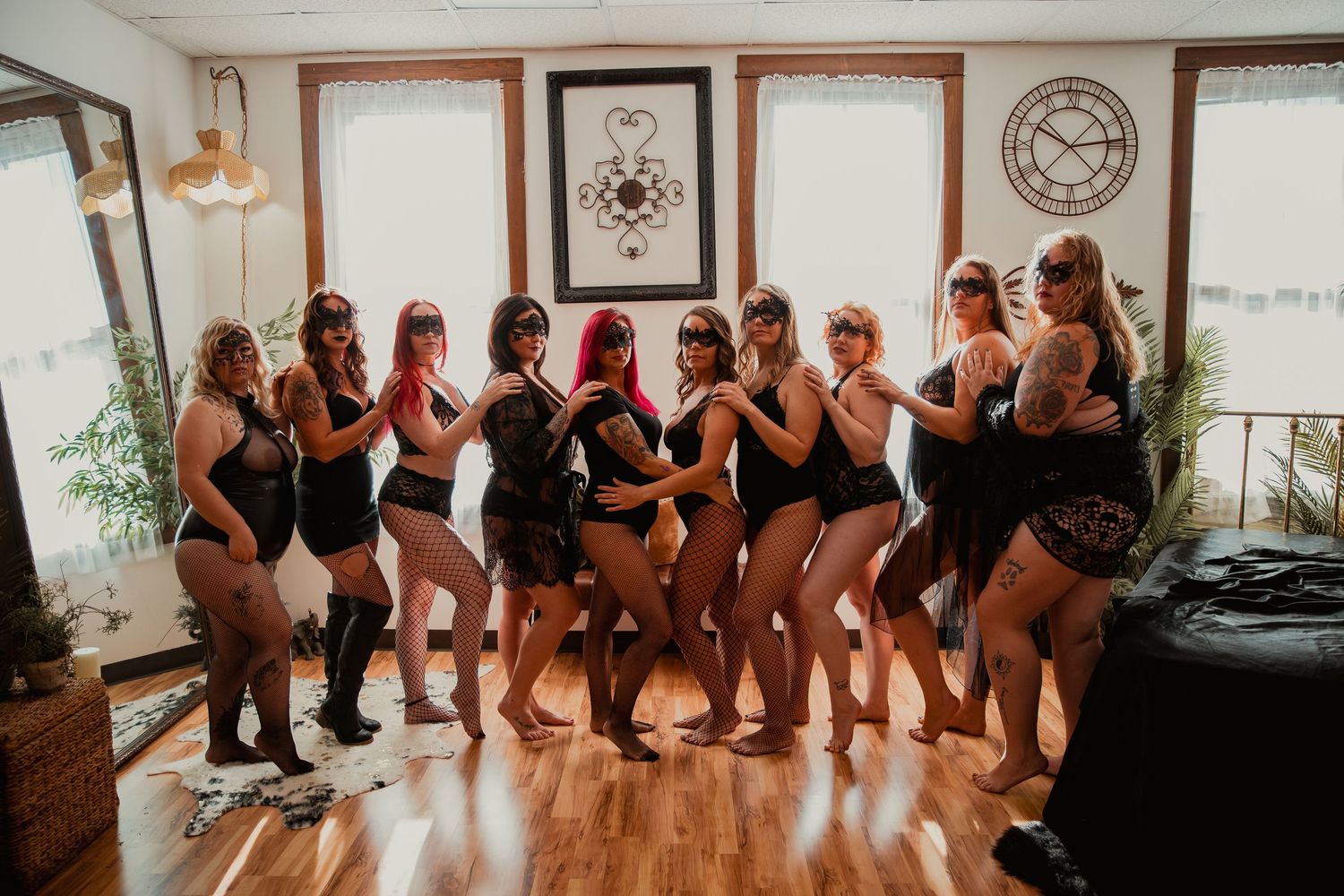 A group in matching black activewear poses together in a sunlit studio with hardwood floors and decorative wall art.