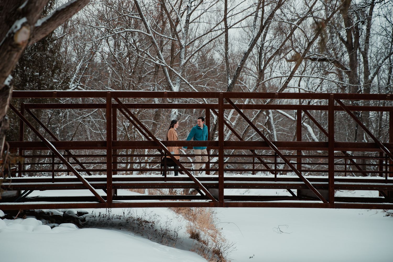 A couple shares a romantic moment on a rustic wooden bridge in winter. couples engagement