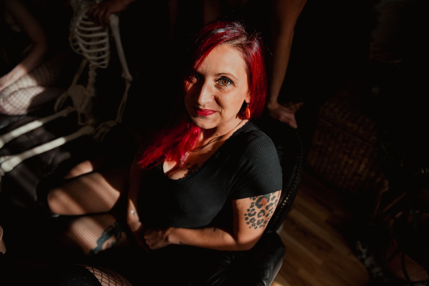 An alternative style portrait in dark moody lighting features someone with bright red hair wearing a black outfit.