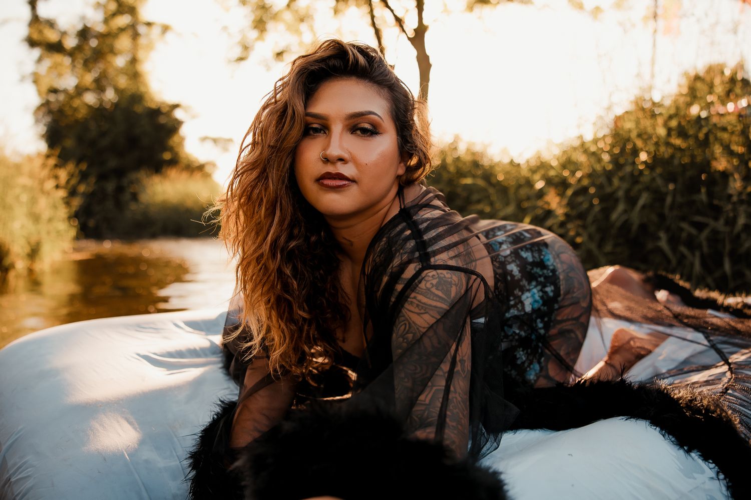 Young model in a floral dress poses outdoors during golden hour with atmospheric sunlight filtering through trees.