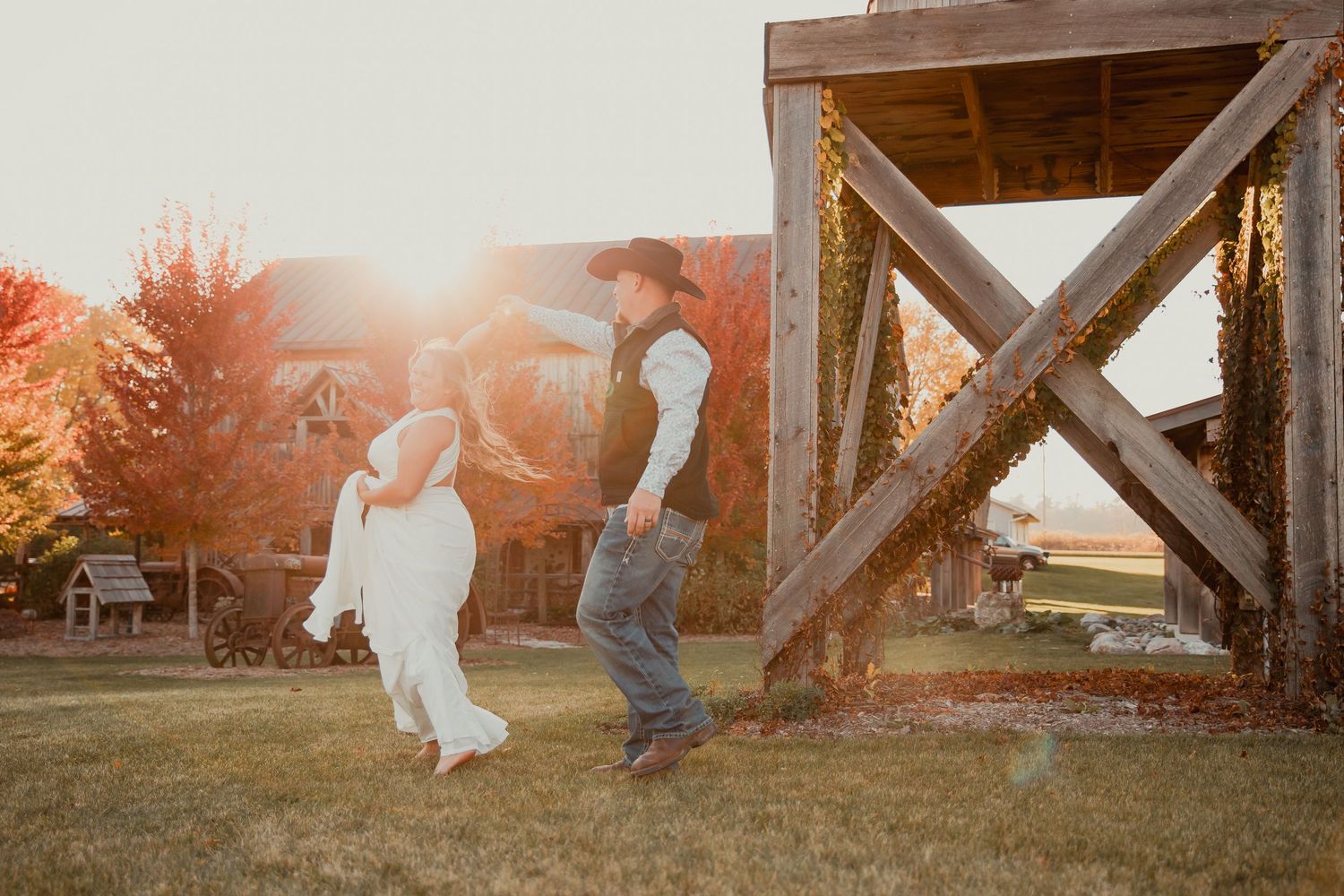Playful couple in wedding attire running through a wooden barn doorway at sunset. wedding