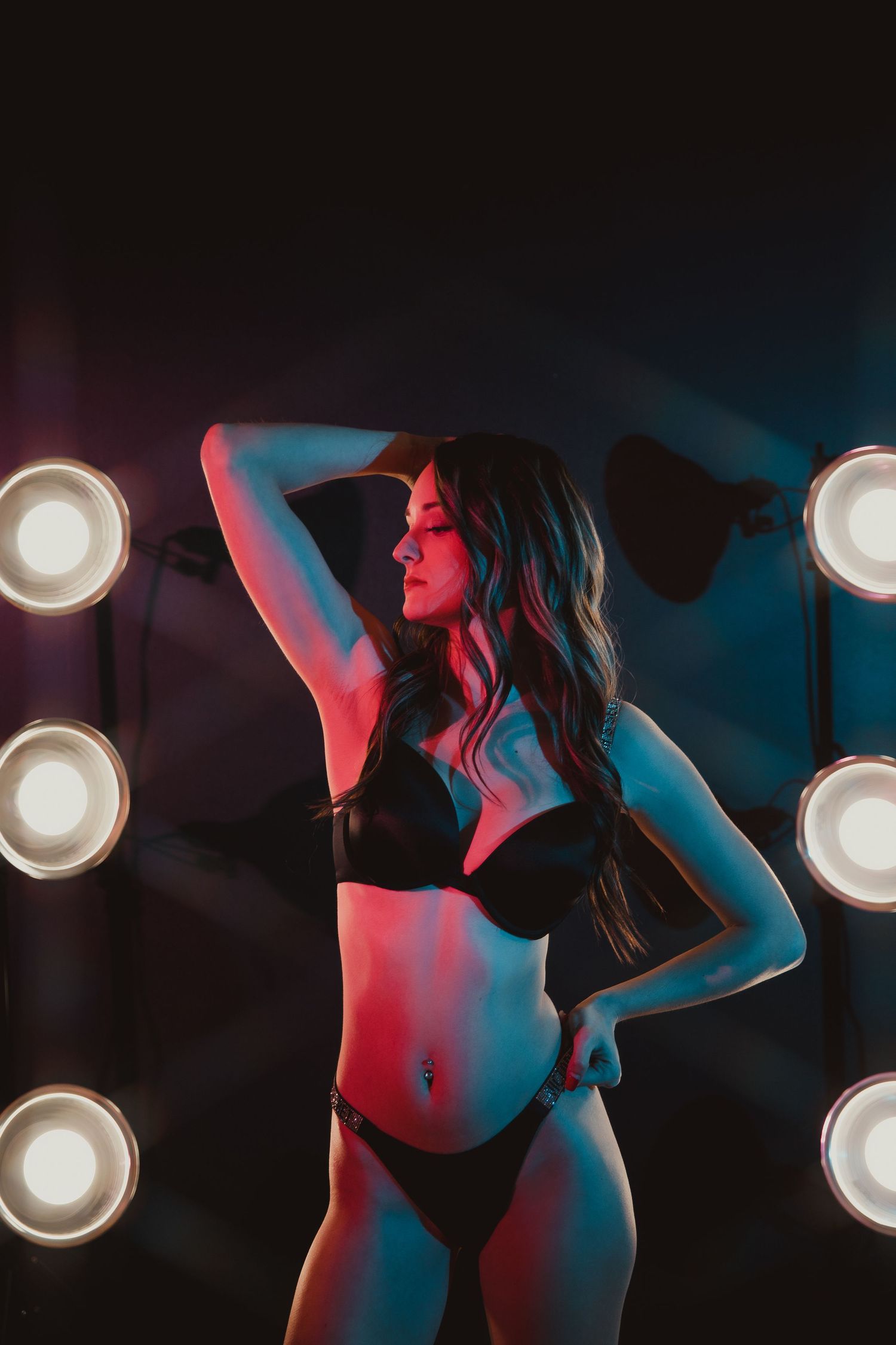Artistic boudoir photo with dramatic lighting showing a silhouette against bright spotlights in red and blue tones.