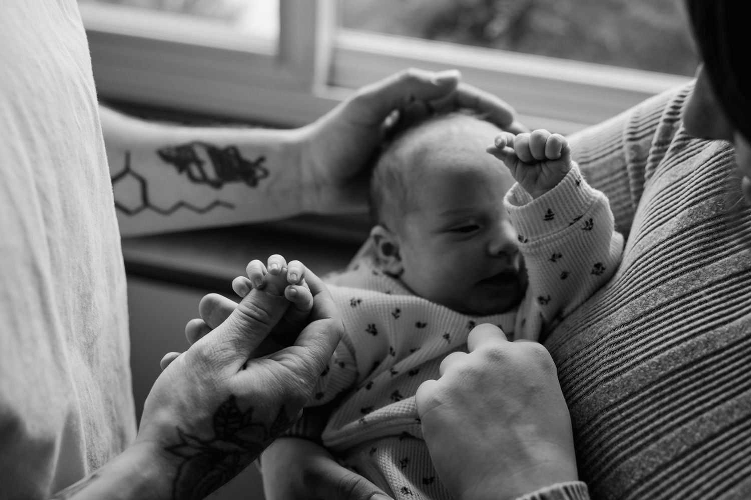 A black and white photo shows a baby being held in someone's arms while wearing a patterned onesie.