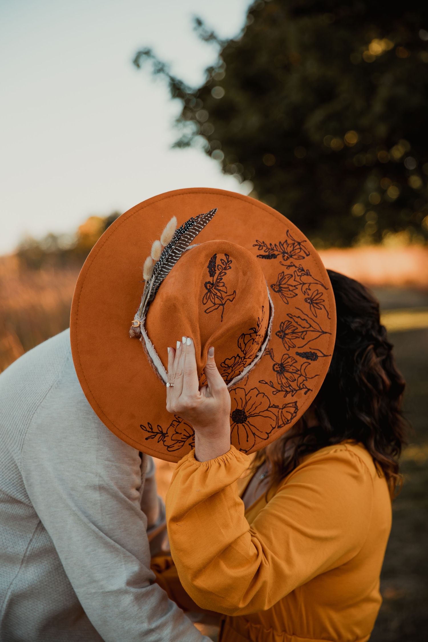 A couple sharing a romantic kiss behind a decorative orange hat in warm autumn sunlight. couples engagement