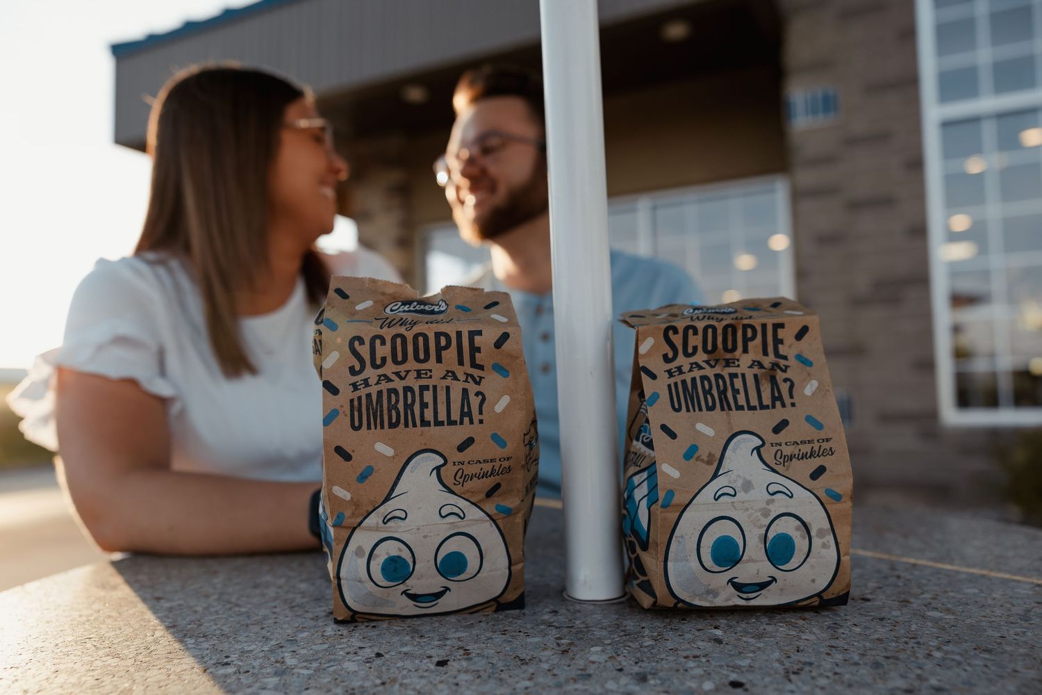 Couple sitting behind two Scoopie umbrella ice cream bags on a concrete ledge at golden hour.