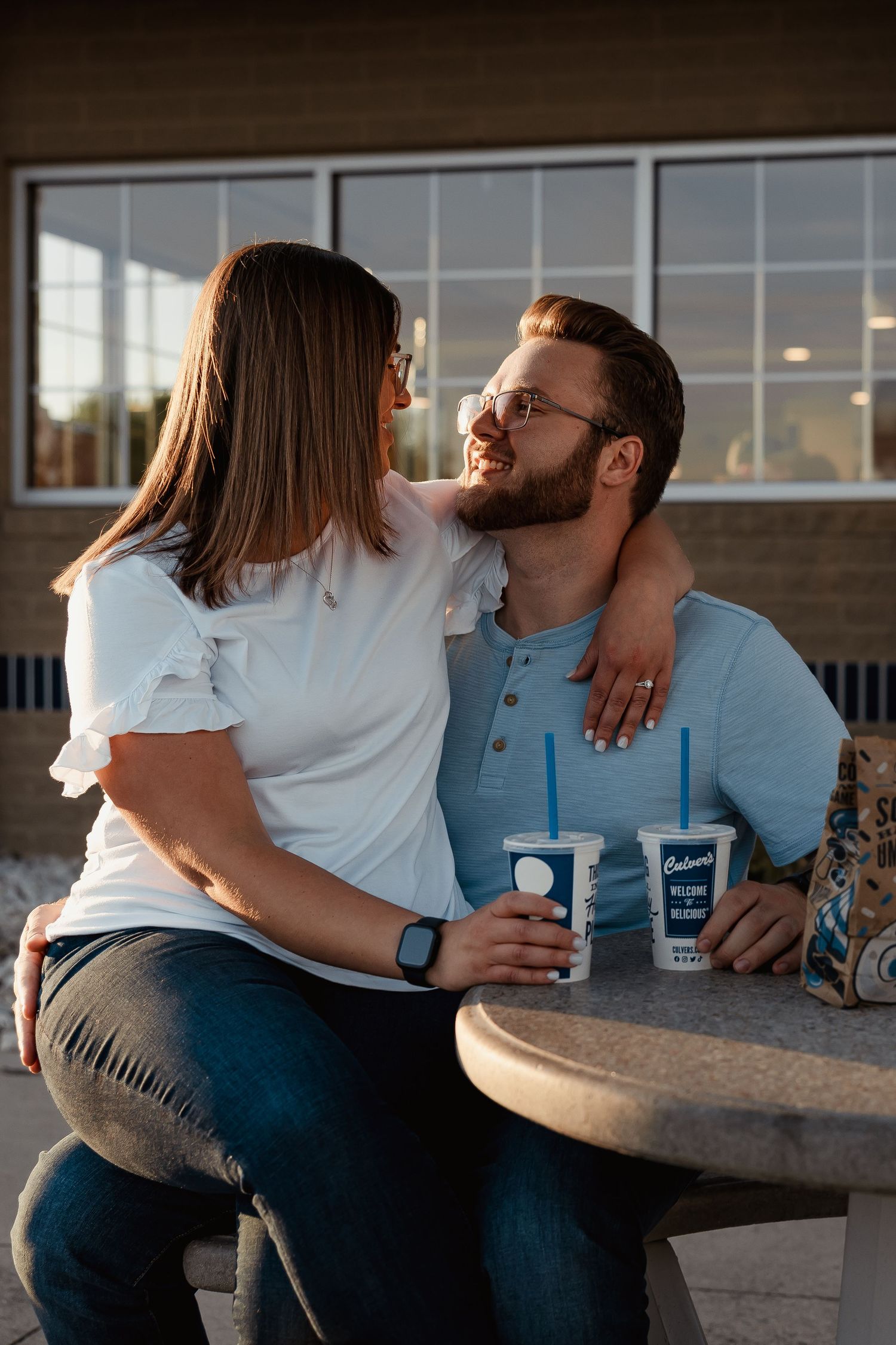 Couple embracing at outdoor Culvers table with frozen custard drinks during golden hour.