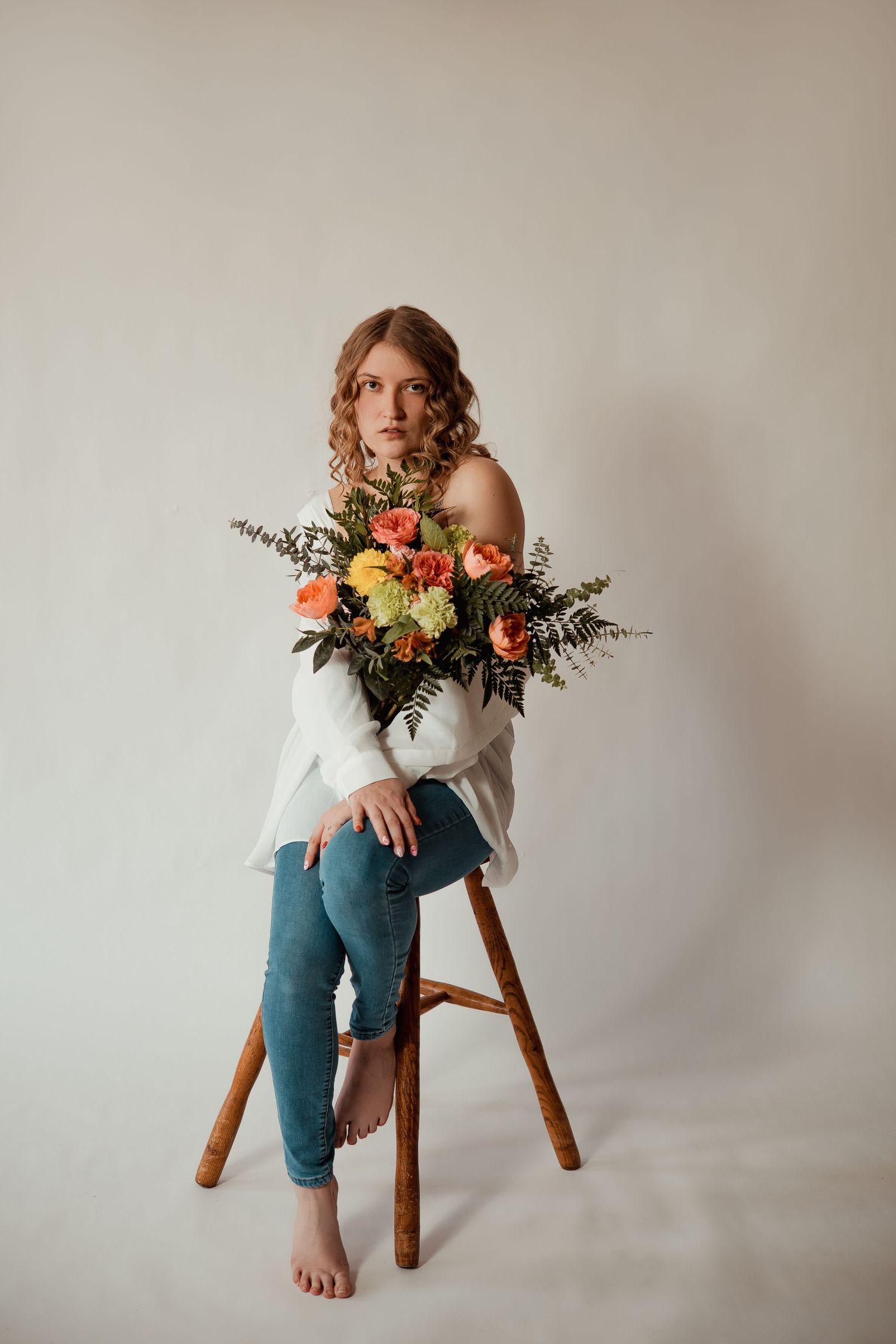 A person in jeans sits on a wooden stool with vibrant floral arrangements featuring orange and yellow blooms.